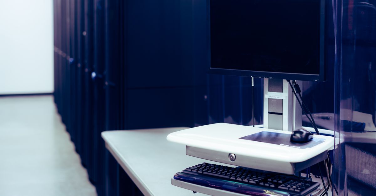 Contemporary computer with black screen placed on stand near row of server steel racks in data center