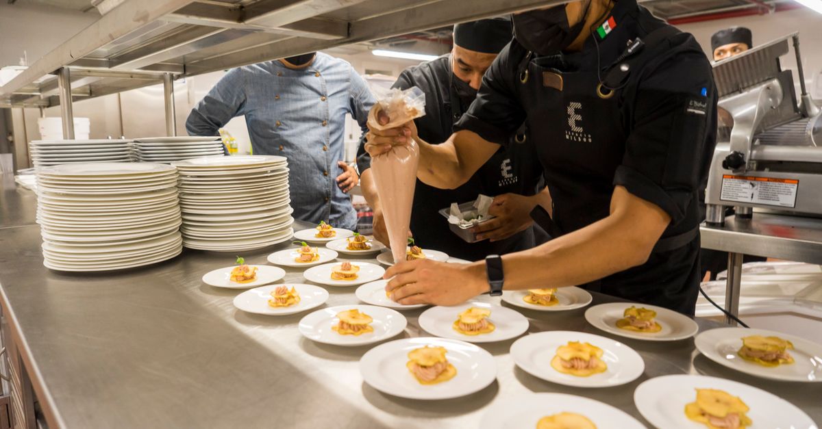 Chefs work meticulously plating gourmet dishes in a bustling professional kitchen.