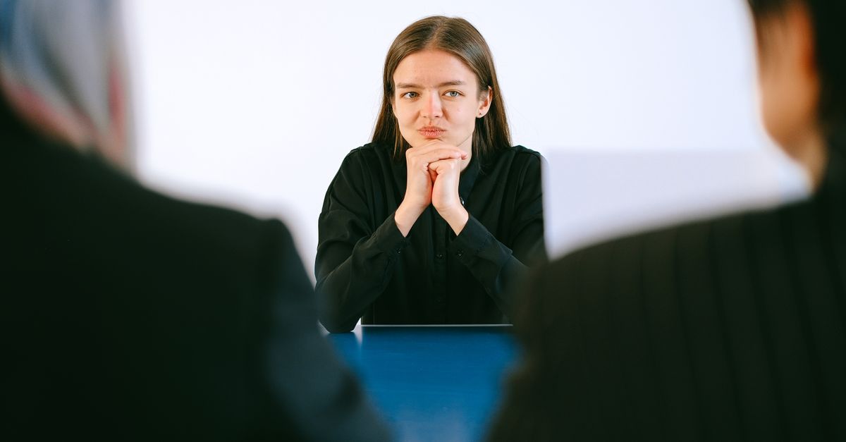 A woman in a job interview facing two people at an office table, focusing intently.