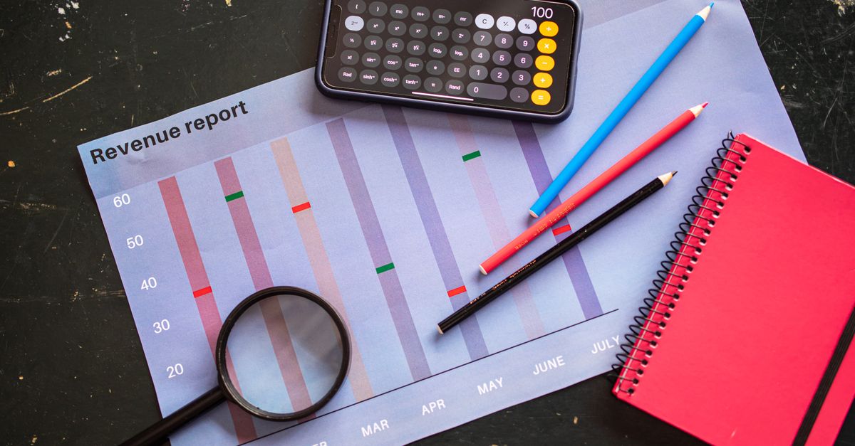 Flat lay of revenue report with a calculator, pencils, and notebook.