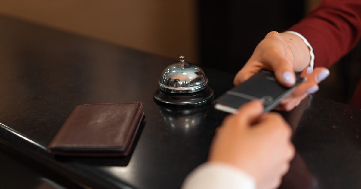 A close-up of a hotel check-in process with a smartphone and card transaction at the reception desk.