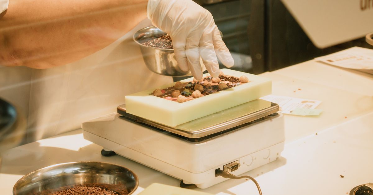 Chef in gloves arranging chocolate and ingredients on a kitchen scale for confectionery preparation.