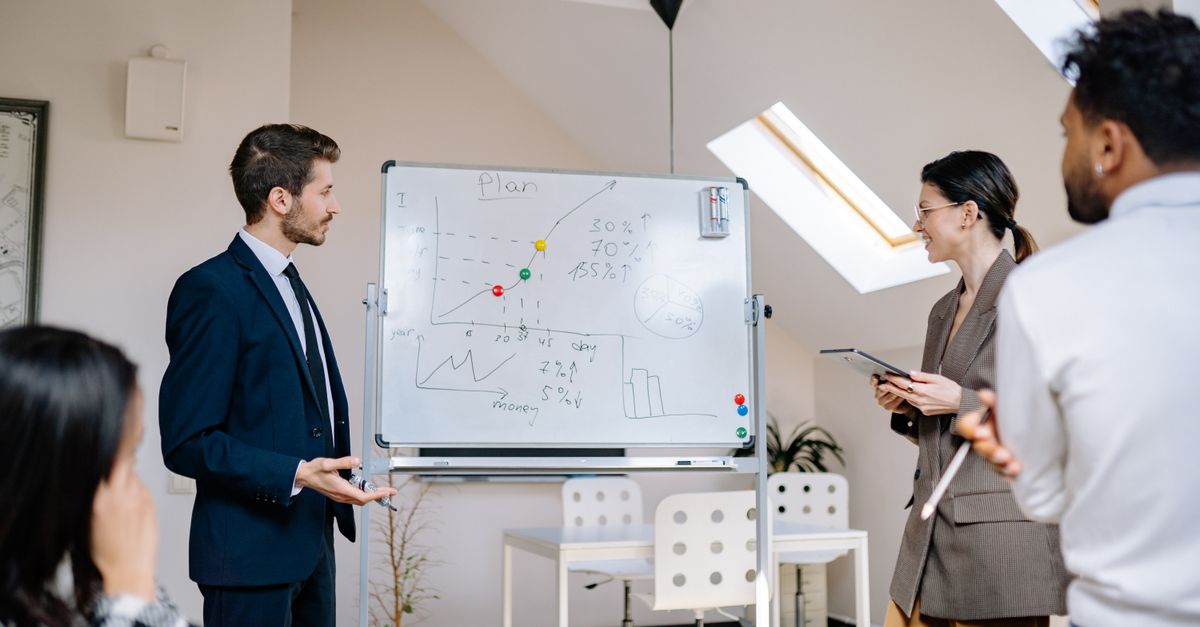 Colleagues collaborating at a business meeting, analyzing graphs on a whiteboard.