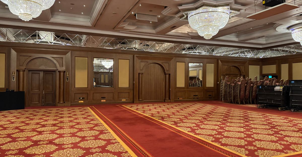 Spacious banquet hall with luxurious chandeliers and red carpet flooring.