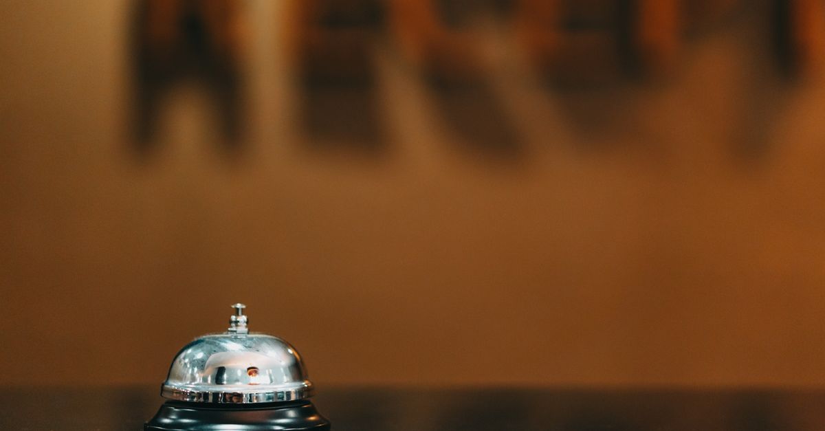 Close-up image of a silver hotel bell on a black surface with 'RECEPTION' blurred in the background.
