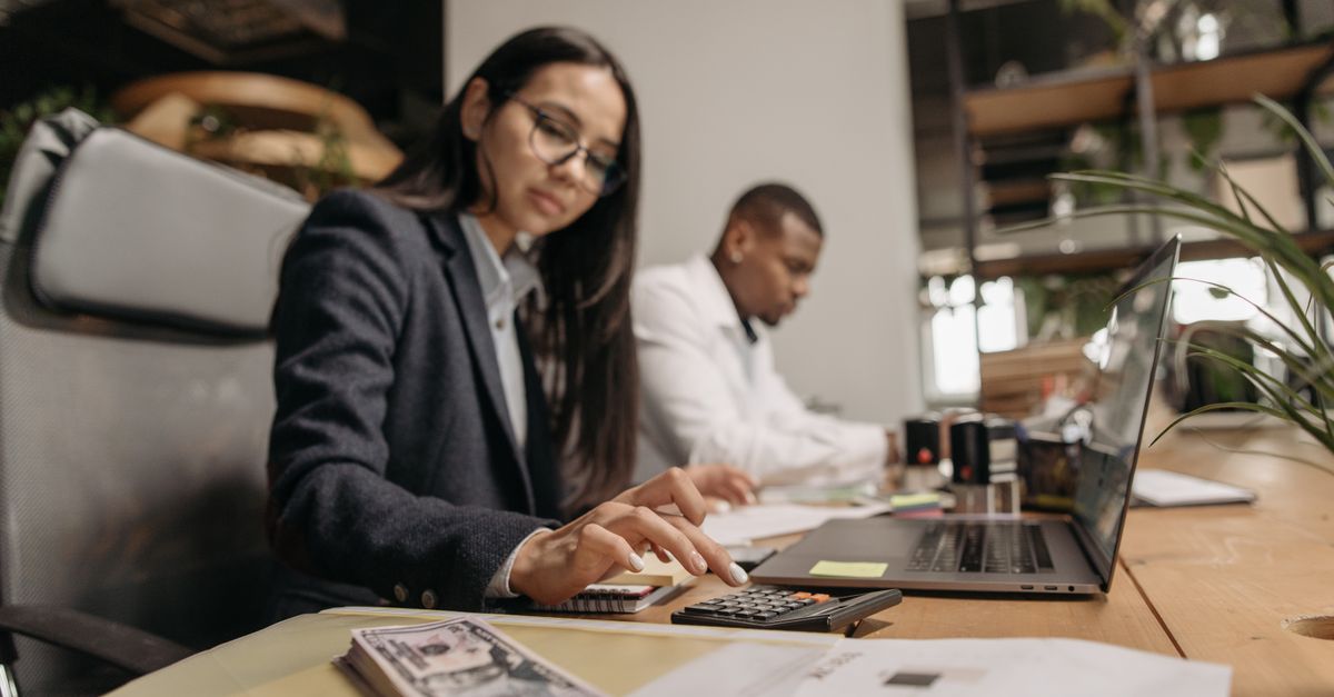 Two business professionals collaborating with a laptop and calculator in a modern office.