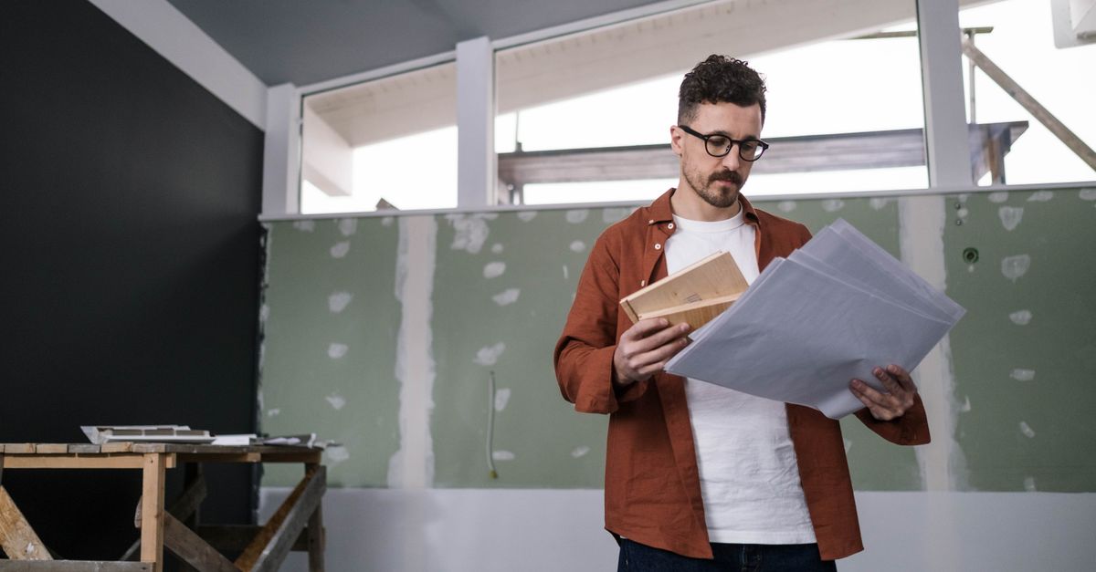 A focused adult male architect examines construction plans indoors, showcasing project management.