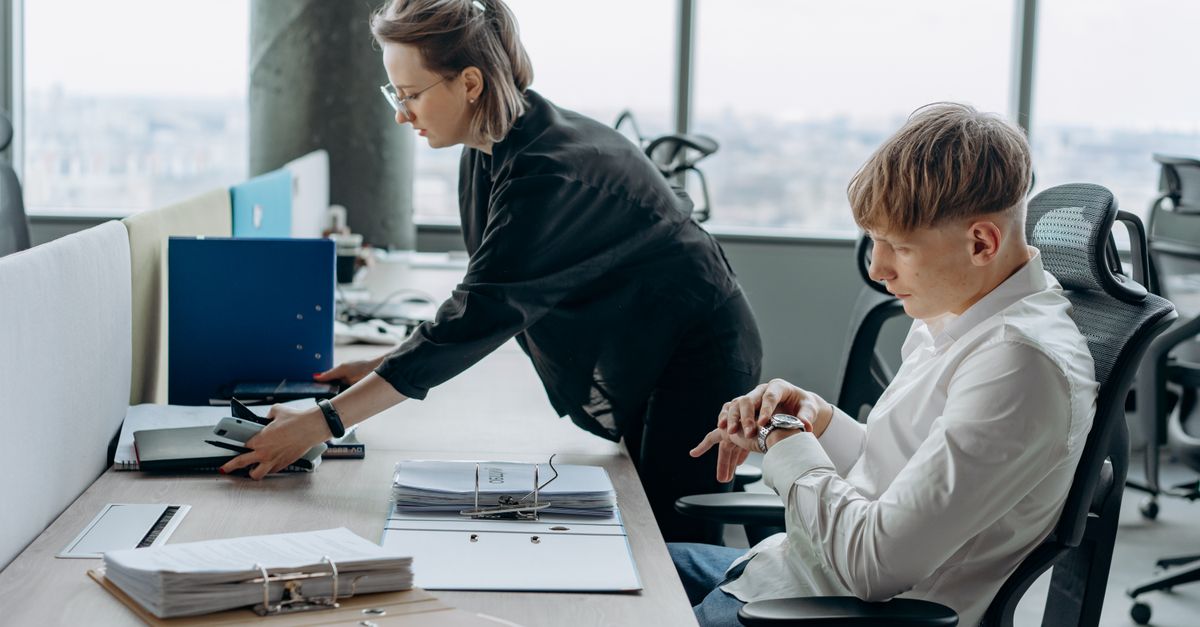 Two business professionals working together in a modern office environment with documents and computers.