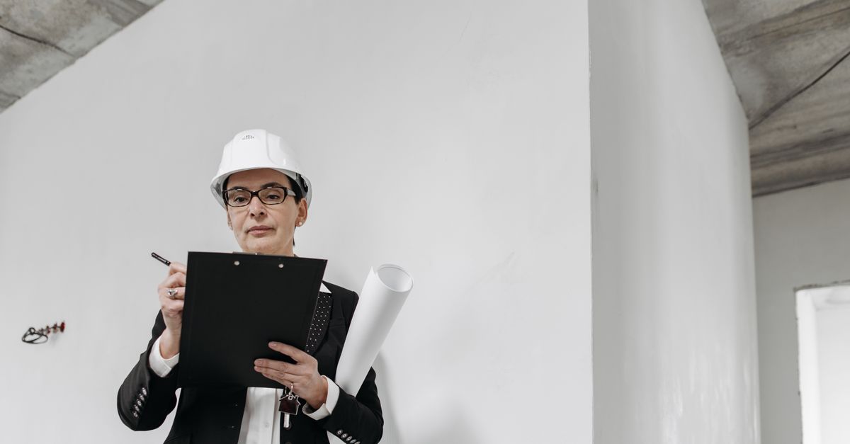 A female engineer in a hard hat reviews building plans with focus.