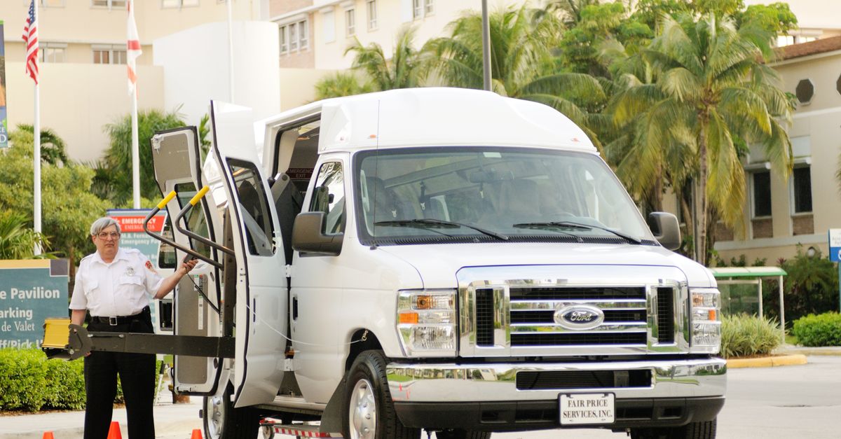 A parking assistant operating a van with a wheelchair lift in a palm-lined parking area.