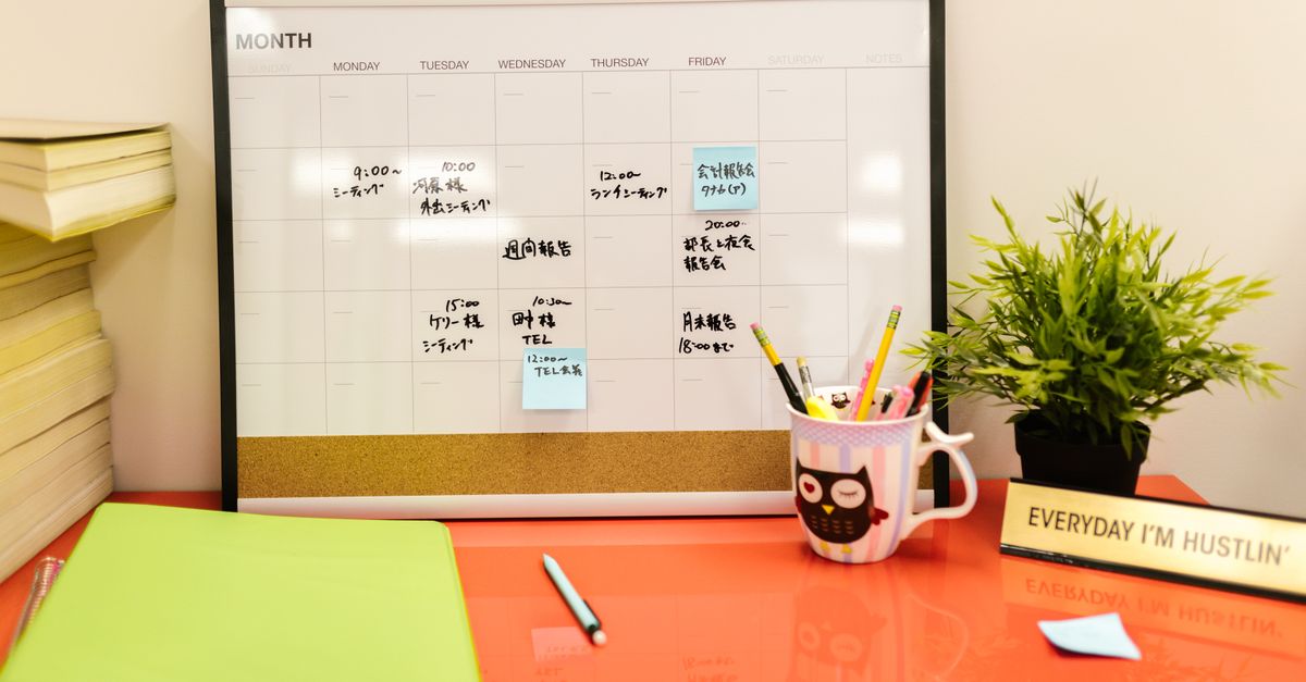 Neat workspace with a calendar, plant, and stationery on a red desk.