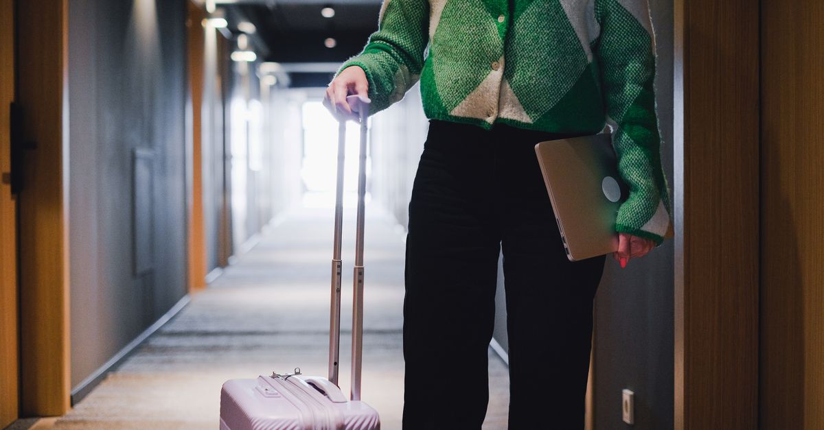 A person in a hotel corridor holding luggage and a laptop, showcasing travel and business.