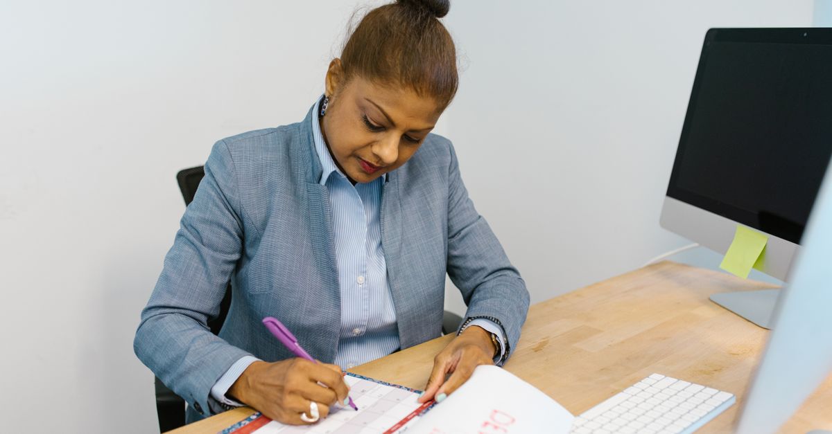 Businesswoman writing plans in a calendar at her office desk.