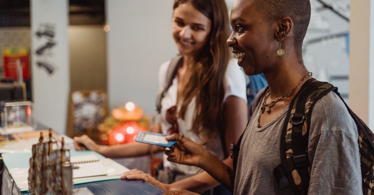 Two travelers check in at a hotel reception, smiling and engaging with the staff.