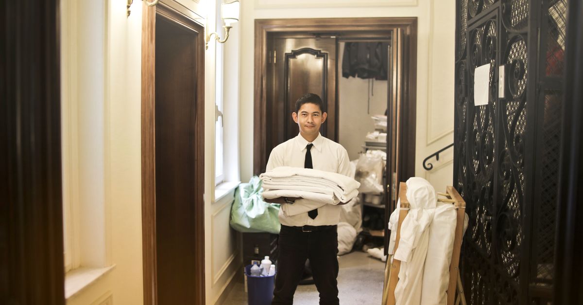 Professional hotel staff member carrying fresh linens in an elegant hallway.