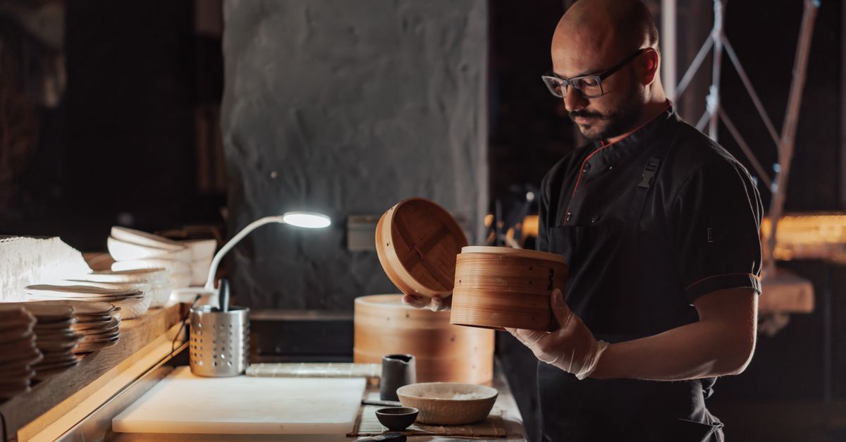 A chef skillfully prepares dim sum in a traditional bamboo steamer in a restaurant kitchen.